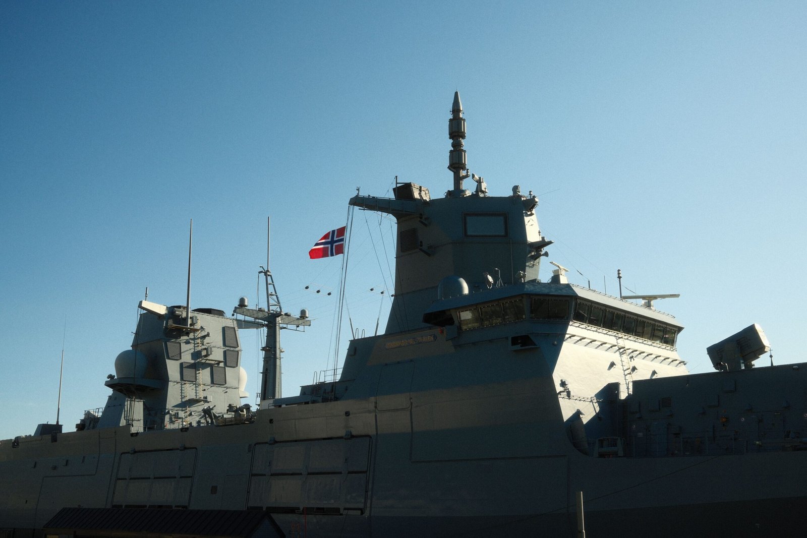 Grey naval frigate sailing under a blue sky