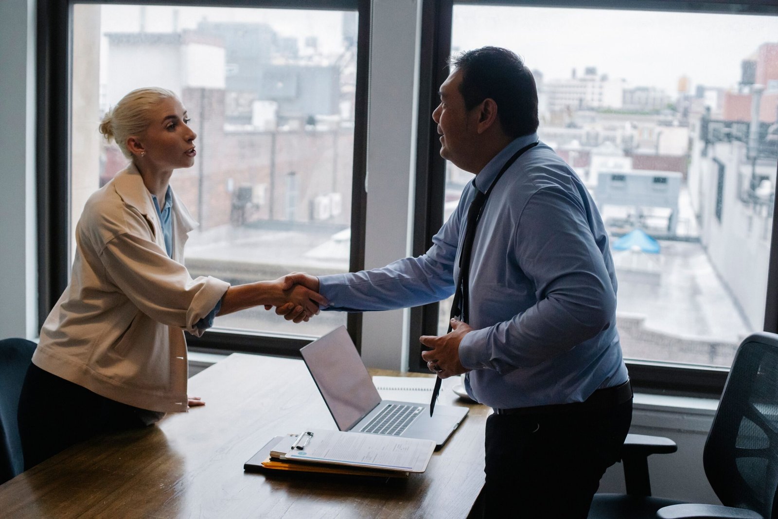 Young woman shaking hands with employer after a successful job interview, representing thank you email etiquette after interviews